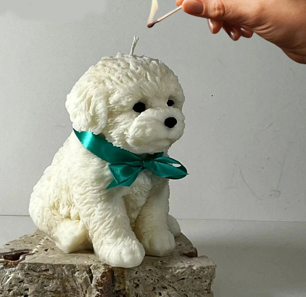 Candelina artigianale a forma di cagnolino bianco con nastro verde, accesa con un fiammifero.